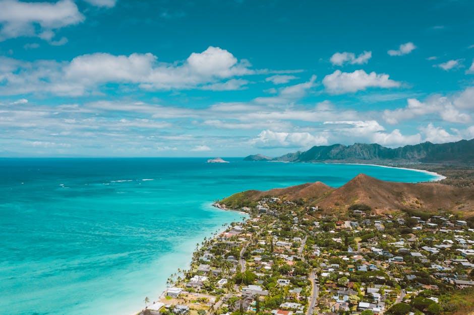 A scenic aerial shot of a tropical town by the ocean with turquoise waters and mountain ranges.