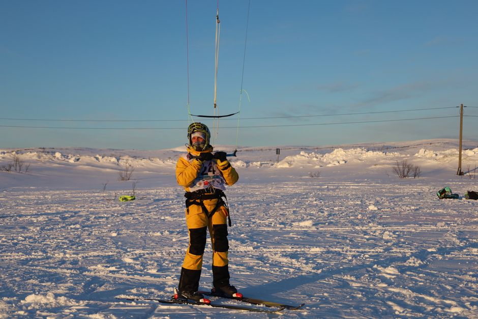 Snowkiter in vibrant outfit navigating snowy terrain under clear skies.