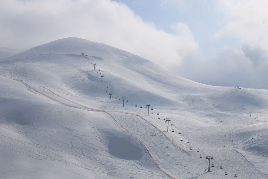 Aerial view of a snowy mountain ski slope with a chairlift under cloudy skies.