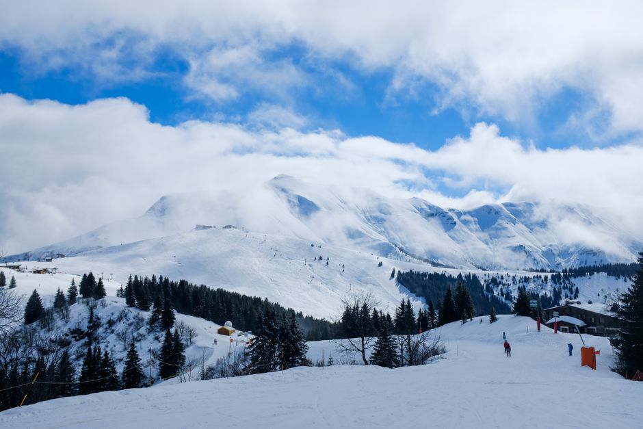 Beautiful winter mountain scene with skiers, trees, and snow-covered peaks.