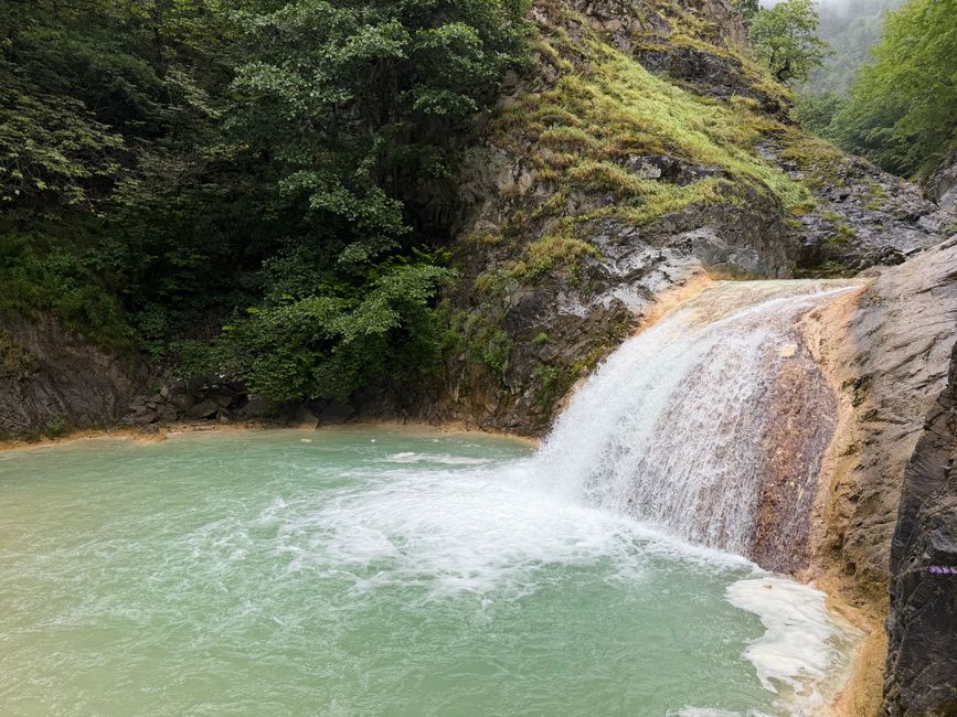 A tranquil waterfall cascading into a turquoise pool surrounded by lush greenery.