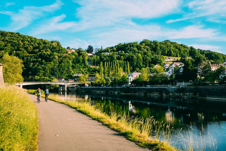 Two cyclists enjoying a ride along a picturesque riverside pathway with lush green hills in summer.