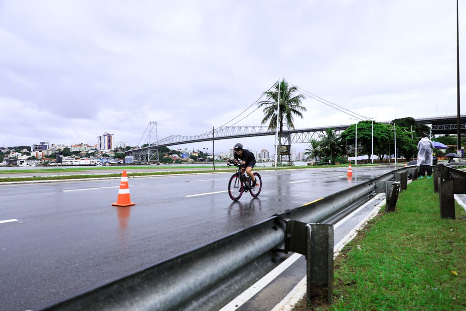 Cyclist racing on a wet road near prominent bridge in cityscape setting.