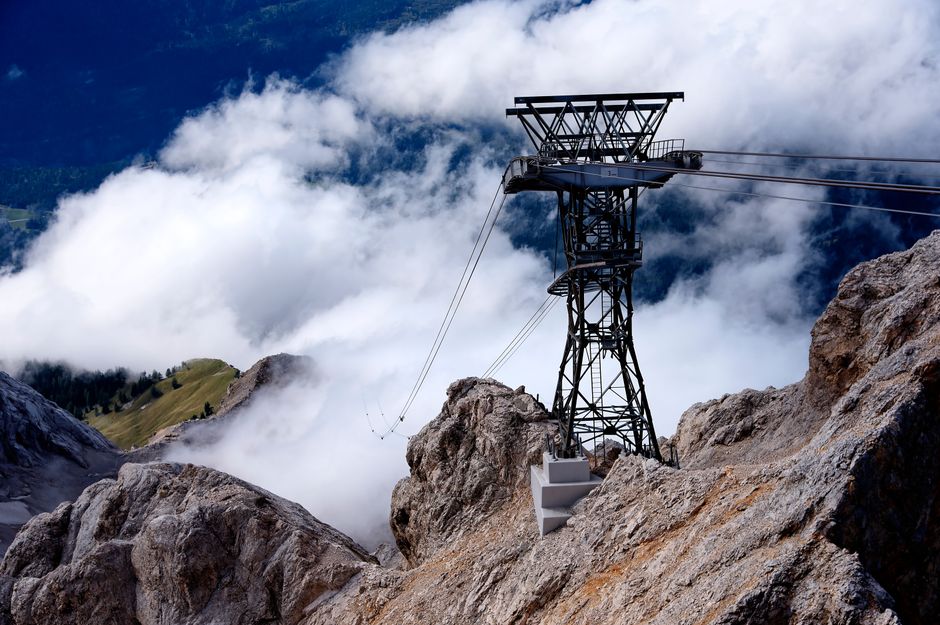 A majestic view of rugged mountain peaks shrouded in clouds with a cable car support tower.