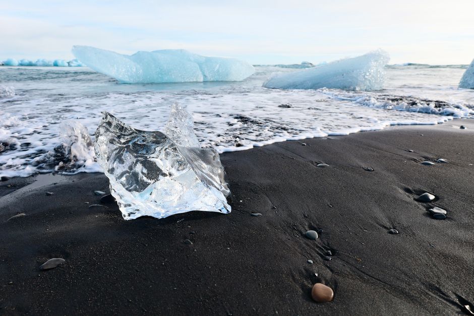 Glacier ice on the black sand beach with sea waves in Iceland.