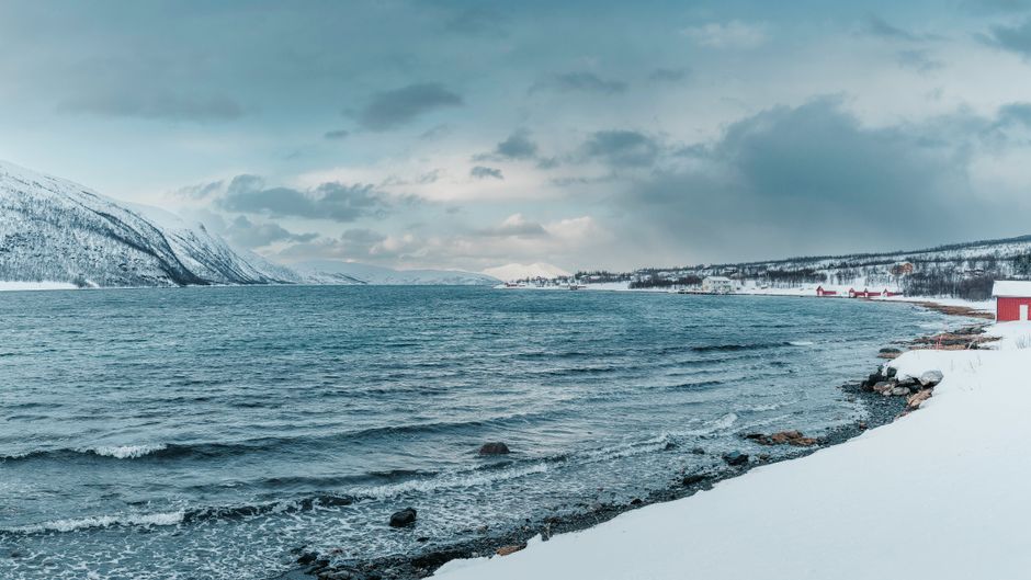 Beautiful snowy coastline with distant mountains and overcast sky in Norway.