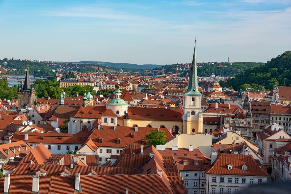 Aerial view of Prague showcasing red rooftops and historic landmarks under a clear blue sky.