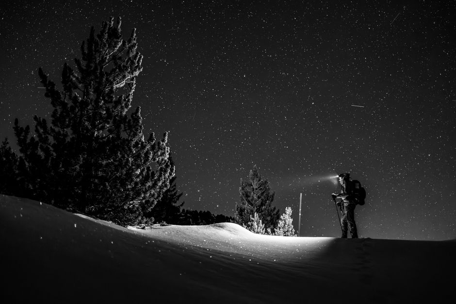 A lone explorer with a flashlight under a starry winter sky and snow-covered landscape.