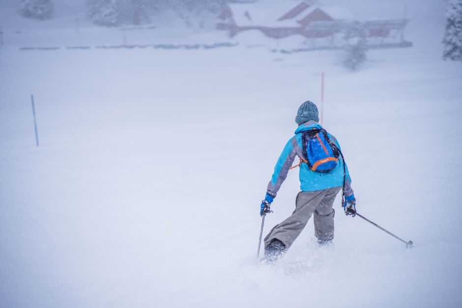 Back view of a man skiing on a snow-covered slope in winter.