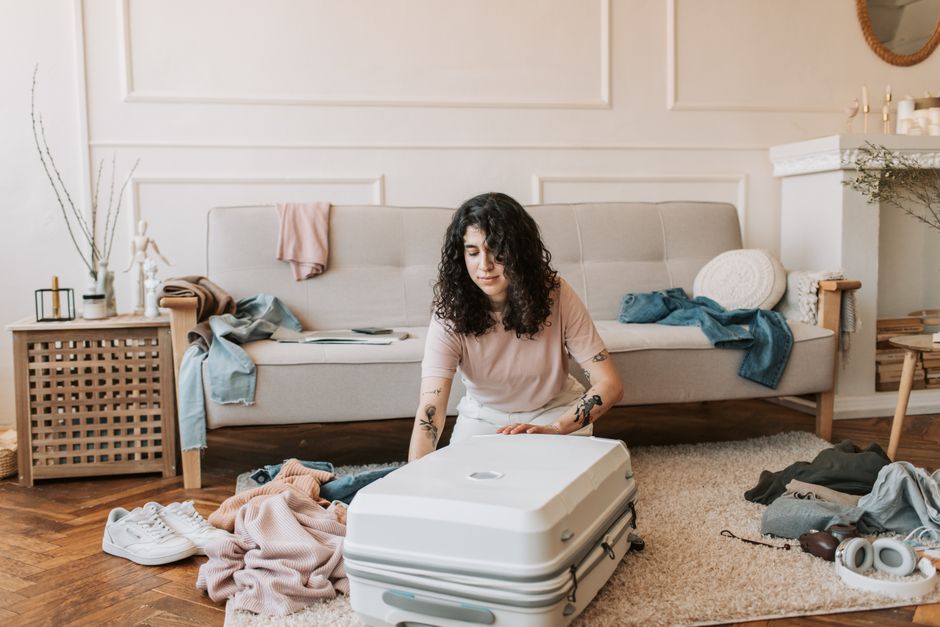Woman with curly hair packing a suitcase in a stylish living room with a modern, cozy vibe.