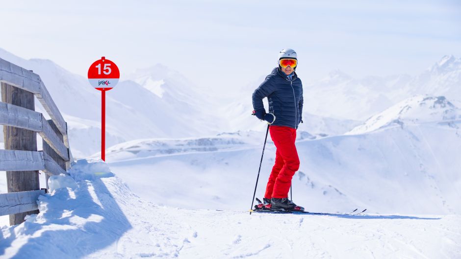Skier at a mountain resort posing with snowy peaks in the background.