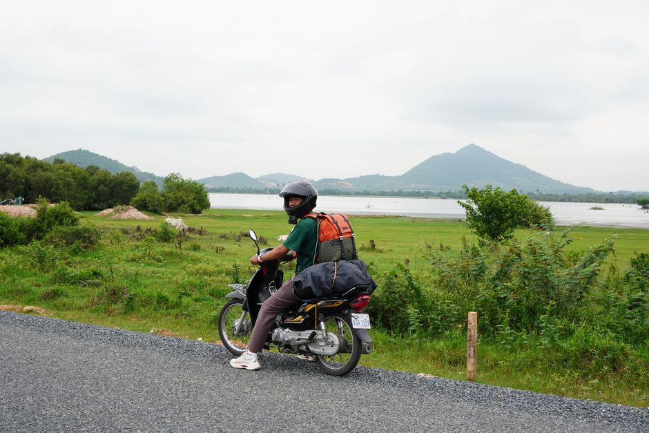 Traveler on a motorbike exploring the scenic landscape of Kampot, Cambodia, with lush greenery and mountains.