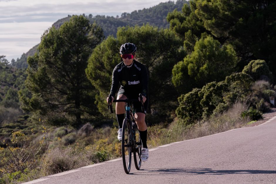 A woman cyclist wearing sportswear rides a road bike on a tree-lined rural path.