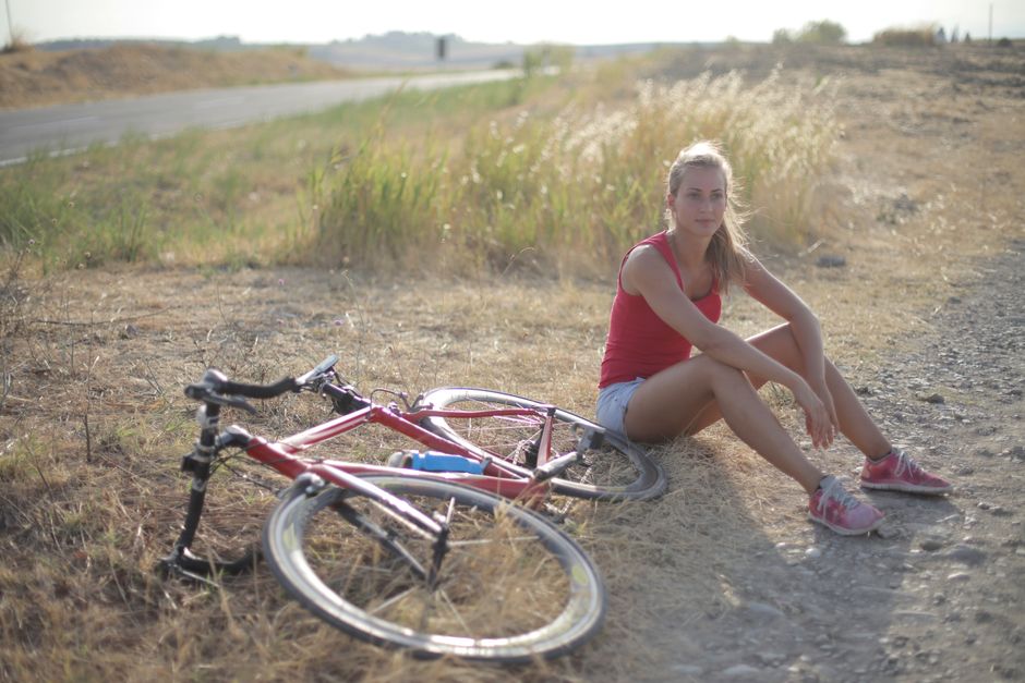 A young woman sitting beside her bicycle in a sunlit grassy field.