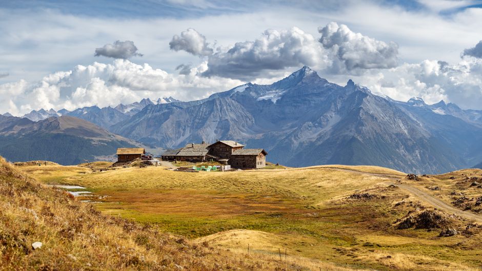 Spectacular view of a rustic alpine cabin against majestic mountain peaks under a dramatic sky.