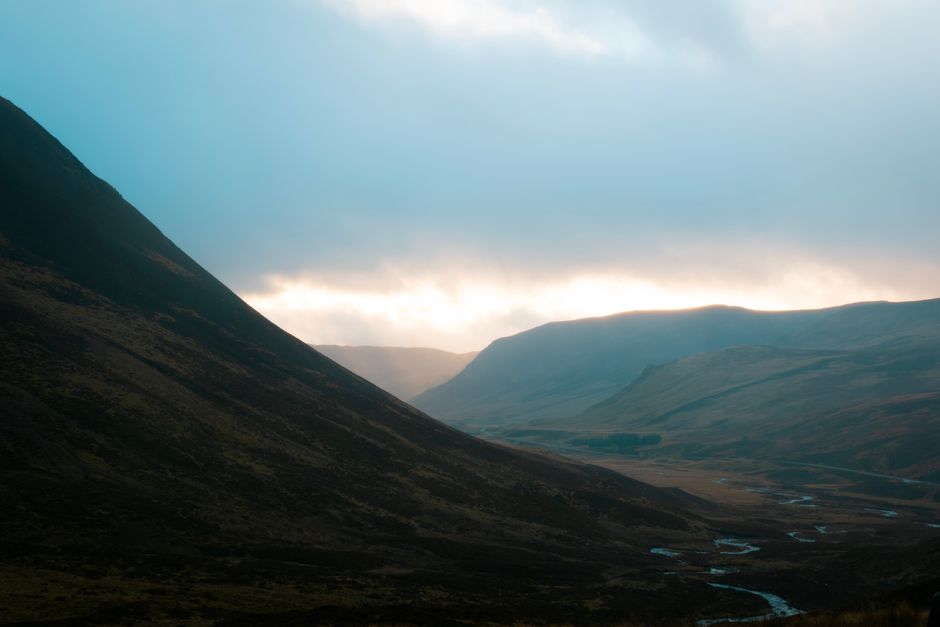 Serene Scottish Highlands landscape with dramatic lighting and misty atmosphere captured at sunrise.