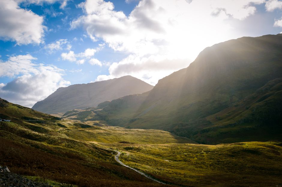 Dramatic view of the Scottish Highlands with sunbeams over lush green valleys and majestic mountains.
